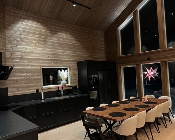 Denna moderna tappning på den klassiska fjällstugan beställdes av kund som ett fritidsboenden på en av Sveriges populära skidorter.
Huset är utvändigt klätt med svart panel och invändigt med en mörkbrun murrig panel. Den höga fönsterbeklädda gaveln vetter ut mot skidbacken och ger en vacker vidsträckt utsikt över landskapet från både allrummet och från loftets balkong. Den centrerade kaminen förstärker rummets höjd när det leder ögat upp.